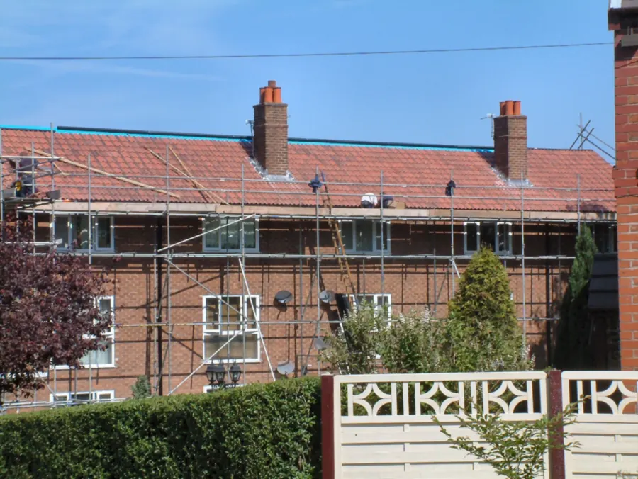 Row of brick houses with scaffolding while the red tiled roof is replaced like for like
