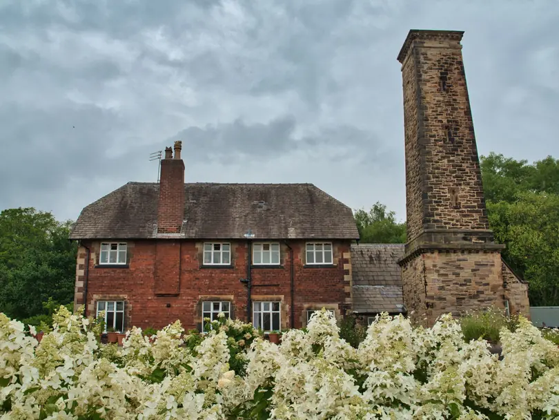 Red brick house with a tall brick chimney stack rising through a weathered stone slate roof on an overcast day
