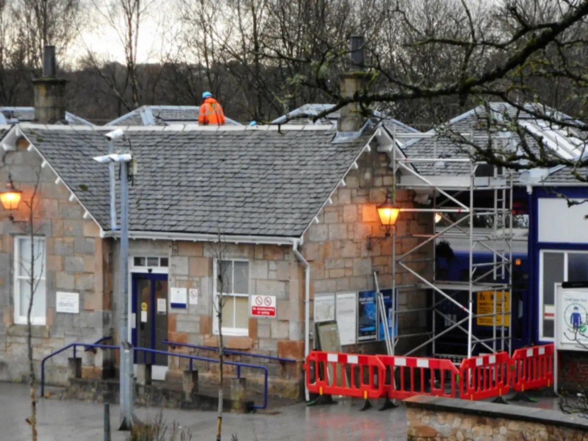 Roofer in orange hi-vis working on a grey slate roof of a stone building during roof repairs