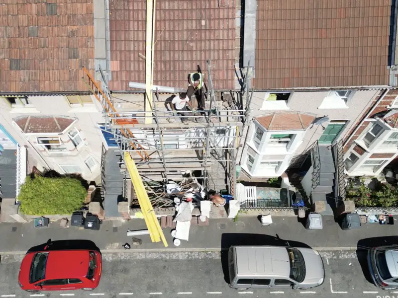 Roofers on the scaffold at the front of a terraced house, loading out materials for a re-roof