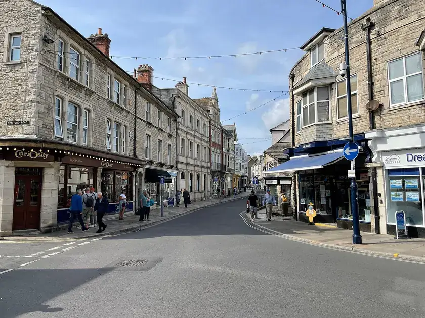 Shops and stone buildings with pitched roofs looking up Swanage High Street
