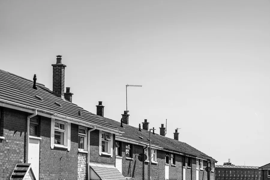 Black and white view of a brick terrace with white uPVC guttering, downpipes and a run of chimney stacks along the roofline